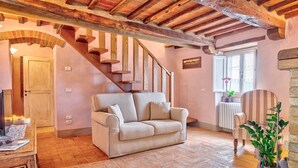 Un salon chaleureux avec un canapé, un escalier en bois, un radiateur et une fenêtre donnant sur un beau paysage.