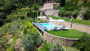 Une villa en pierre dotée d’une piscine, entourée d’une végétation luxuriante et accessible par un escalier en pierre menant à l’entrée.