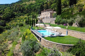 Une villa en pierre dotĂ©e dâune piscine, entourĂ©e dâune vĂ©gĂ©tation luxuriante et accessible par un escalier en pierre menant Ă lâentrĂ©e.