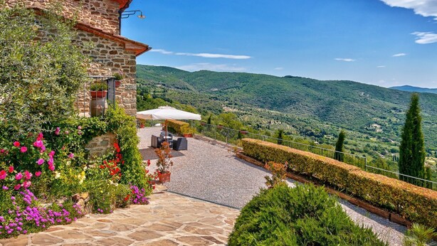 Un bâtiment en pierre doté d’une terrasse, de sièges en plein air et offrant une vue sur des collines verdoyantes.