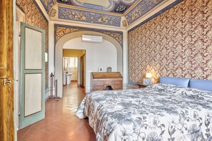 Ein Schlafzimmer mit einem Bett, einer Kommode und einer rundbogigen Tür zu einem Badezimmer.