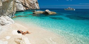 A beach with clear turquoise water, a rocky cliff, and a boat in the distance. - Bari Sardo, Villa with all the amenities near idyllic beaches (FREE Wi-Fi) (Bari Sardo)
