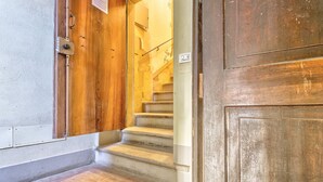 Una puerta de madera con manija metálica, una escalera de piedra y una pared con interruptor de luz.