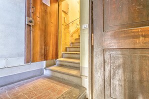 Eine Holztür mit Metallgriff, eine Steintreppe und eine Wand mit Lichtschalter.