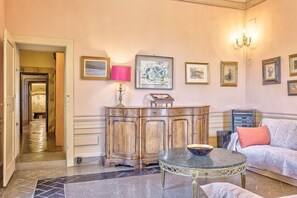 Ein Zimmer mit einem Holzkabinett, einem runden Tisch, einer Couch und gerahmten Kunstwerken an der Wand.