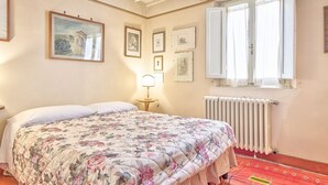 Ein Schlafzimmer mit Bett, Heizkörper, einem Fenster mit Vorhängen und gerahmten Bildern an der Wand.