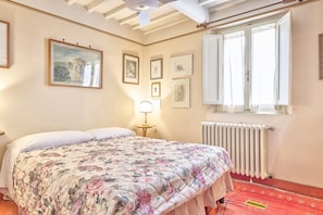 A bedroom with a bed, a radiator, a window with curtains, and framed pictures on the wall.