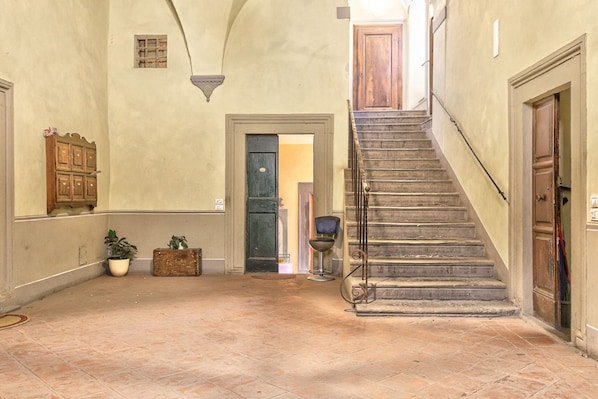 A hallway with a staircase, a wooden cabinet, a potted plant, and a door leading to another room.