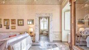 Habitación de hotel con cama, espejo, puerta que da a otra habitación y pasillo con suelo de mármol.