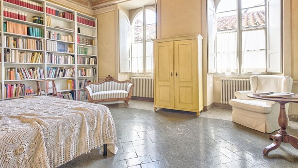 Una biblioteca con estanterías, una cama grande, un sillón de descanso, un armario amarillo y un radiador.