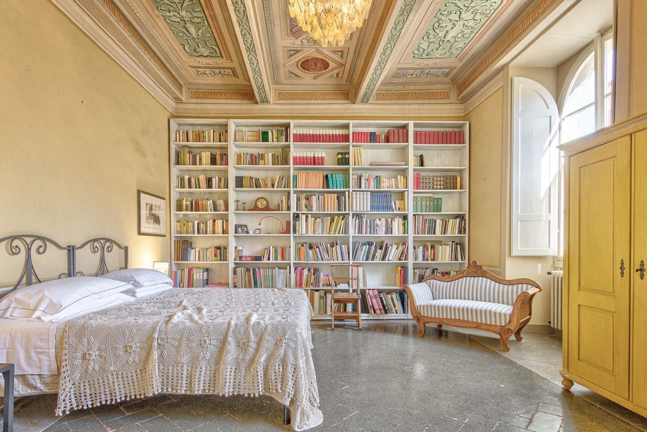 Een kamer met een grote boekenkast, een bed, een stoel en een houten kast.