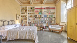 Ein Zimmer mit einem großen Bücherregal, einem Bett, einem Sessel und einem Holzschrank.
