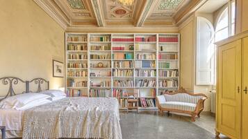 Ein Zimmer mit einem großen Bücherregal, einem Bett, einem Sessel und einem Holzschrank.