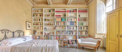 A room with a large bookshelf, a bed, a chair, and a wooden cabinet.