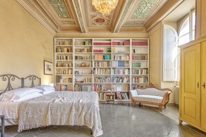 Ein Zimmer mit einem großen Bücherregal, einem Bett, einem Sessel und einem Holzschrank.
