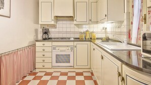 Una cocina con armarios blancos, piso a cuadros, estufa y lavamanos.