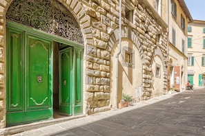 A stone building with green doors, a decorative archway, and a narrow street.