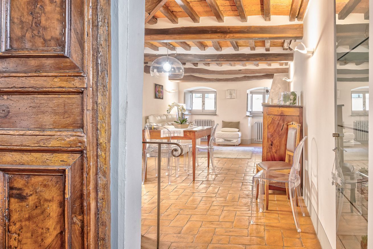 Un intérieur rustique avec des poutres apparentes, un coin repas doté de chaises transparentes et une vue sur la pièce adjacente.