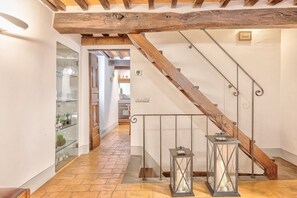 Un escalier doté d’une rampe en bois et de balustrades en métal, menant à un espace cuisine avec vue sur un couloir.
