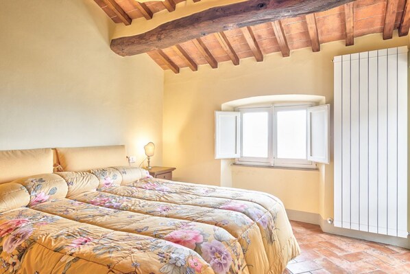 A bedroom with a large bed, wooden ceiling beams, a window, and a radiator.