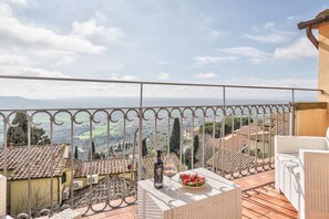 Un balcon donnant sur un paysage vallonné, une bouteille de vin et un panier de fruits.