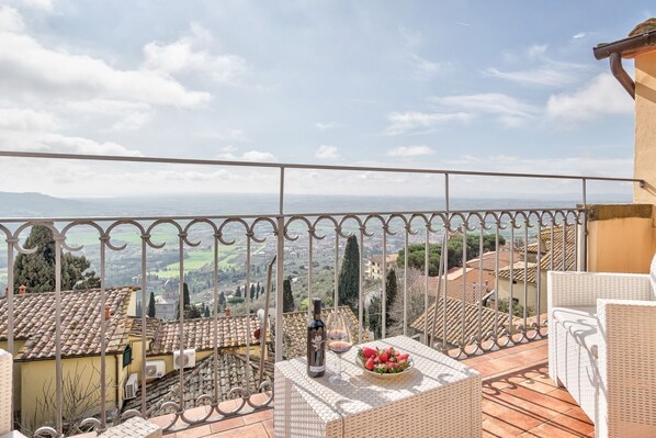 A balcony with a view of a hilly landscape, a bottle of wine, and a bowl of fruit. - La Terrazza - apartment with breathtaking view (Cortona)