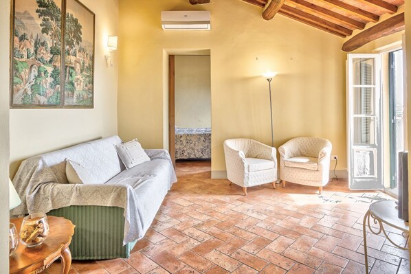 Une pièce comprenant un canapé, deux fauteuils, une lampe sur pied, un tableau et un sol carrelé.