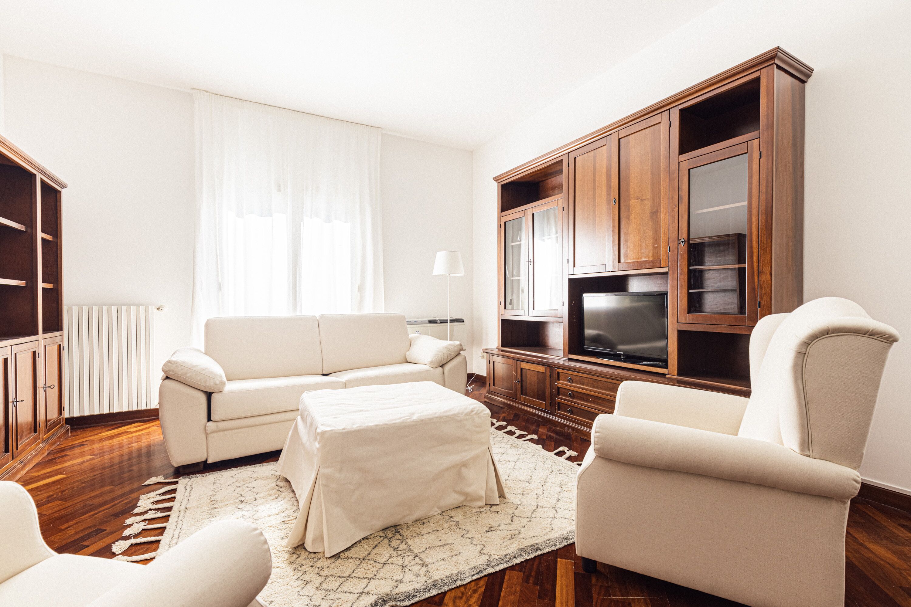 Una sala de estar con sofá, reposapiés y sillones, televisor, aparador de madera y radiador.