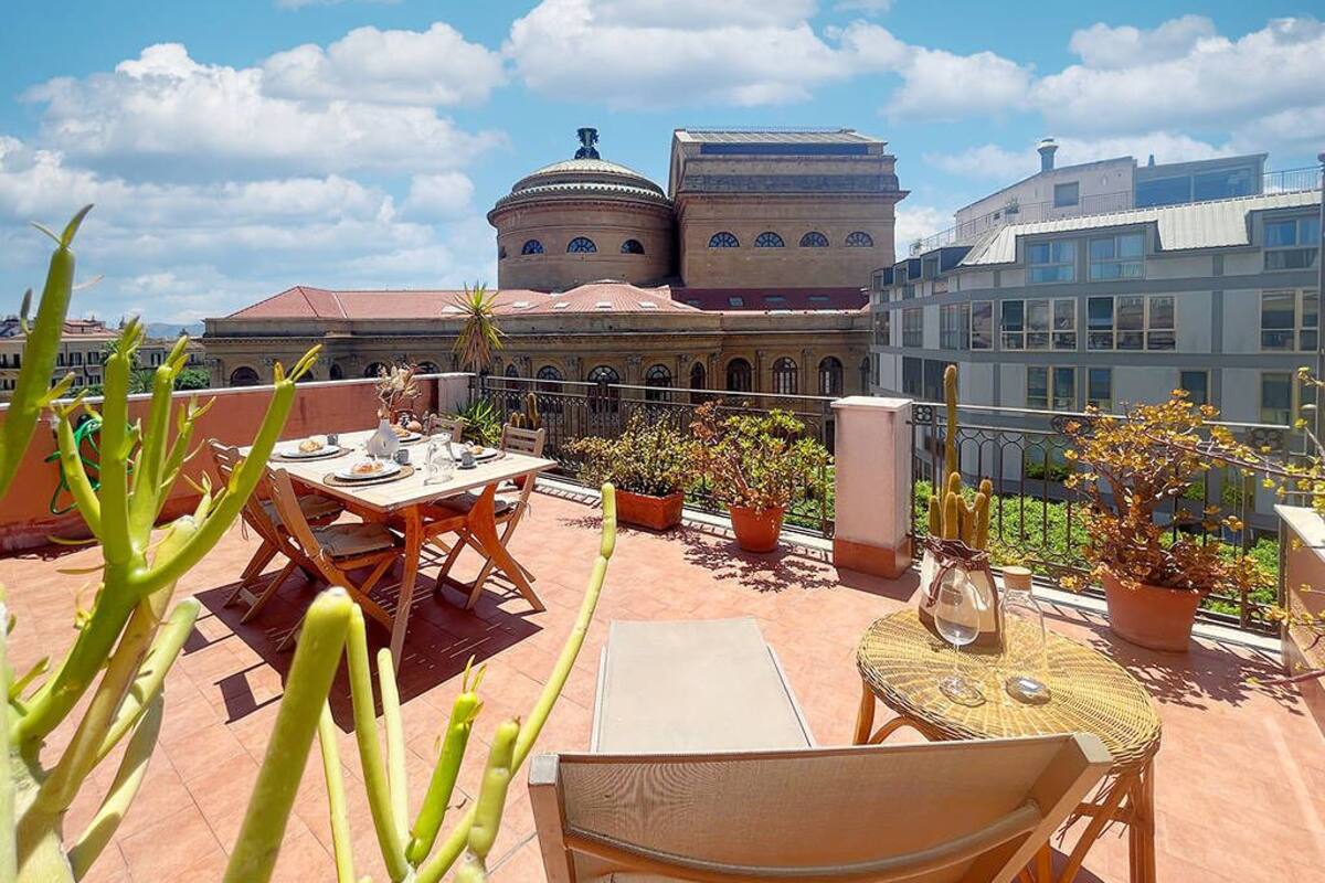 Terraza en la azotea con mobiliario exterior, plantas en macetas y vista a un edificio histórico con cúpulas.