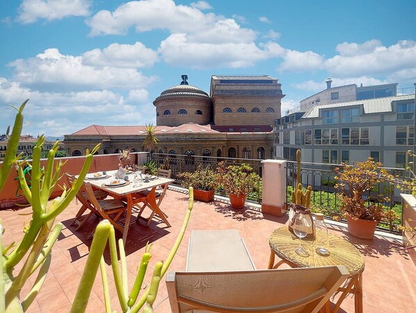 Terraza en la azotea con mobiliario exterior, plantas en macetas y vista a un edificio histórico con cúpulas.