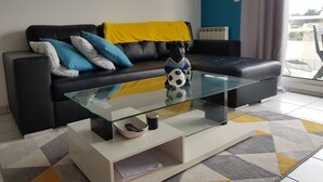 A modern living room with a black leather sofa, a glass coffee table, and a decorative dog figurine. - T1 bis Mezzanine, Très Lumineux, Proche Plage et Commodités (Le Château-d'Olonne)