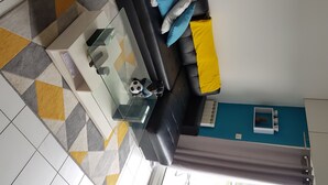 A living room with a black sofa, a glass coffee table, and a patterned rug. - T1 bis Mezzanine, Très Lumineux, Proche Plage et Commodités (Le Château-d'Olonne)