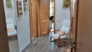 A room with a wooden floor, a bed with a white mattress and a pillow, a wooden chair, a wooden door, and a ceiling with wooden beams. - Ferienwohnung für 2-4 Personen, 1 Sep. Schlafzimmer und Balkon in Chieming-laimgrub (Chieming)