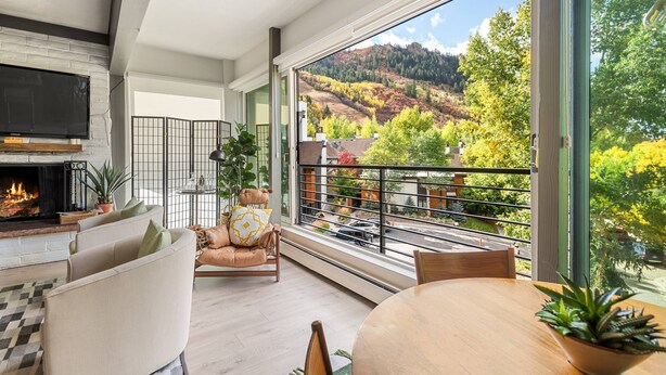 Un salon moderne doté d’une cheminée, de sièges confortables, d’une table à manger et d’une grande fenêtre offrant une vue panoramique sur une colline boisée.