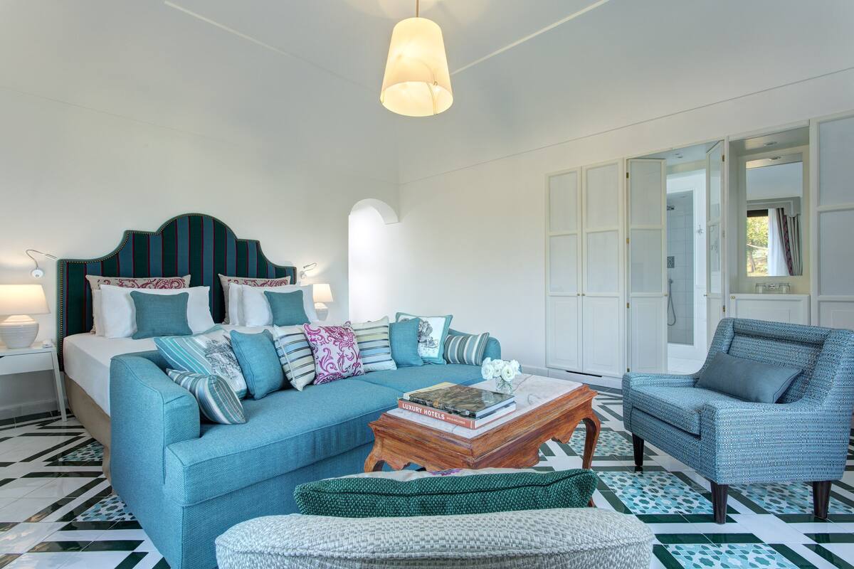 A modern room with a blue sofa, a matching armchair, a wooden coffee table, and a bed with striped headboard.