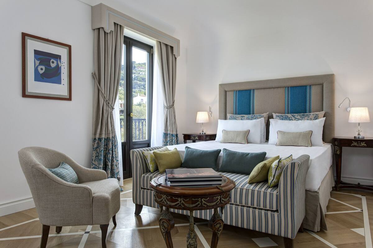 A hotel room with a bed, a chair, a small table, a lamp, and a framed picture on the wall.
