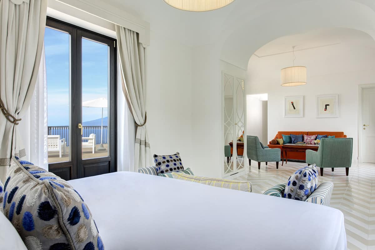 A hotel room with a large bed, a sofa, and a dining area with chairs and a table.