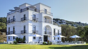 Edifício branco de vários andares com varandas, área de estar ao ar livre e vista para uma colina.