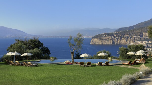 Área de piscina com espreguiçadeiras e guarda-sóis, com vista para a paisagem costeira com falésias e o mar.