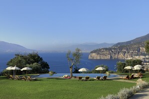 A poolside area with lounge chairs and umbrellas, overlooking a coastal landscape with cliffs and the sea. - Anna Belle Elegant  Agriresort (Sorrento)