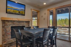 Un comedor con chimenea de piedra, un televisor de pantalla plana grande y vistas a un bosque a través de una puerta corrediza de vidrio.