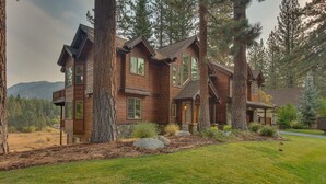 Une grande maison en bois à plusieurs étages, entourée de grands arbres et d’une cour verdoyante.