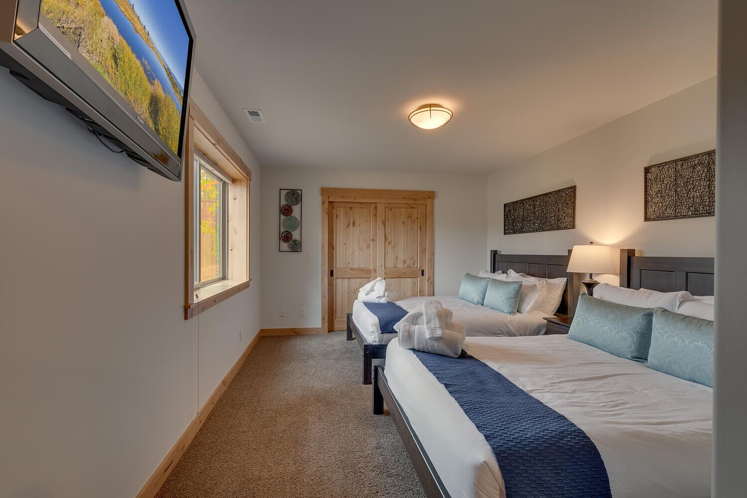 A hotel room with two beds, a TV, a wooden door, and a ceiling light.