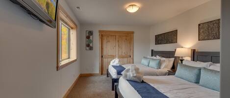 A hotel room with two beds, a TV, a wooden door, and a ceiling light.