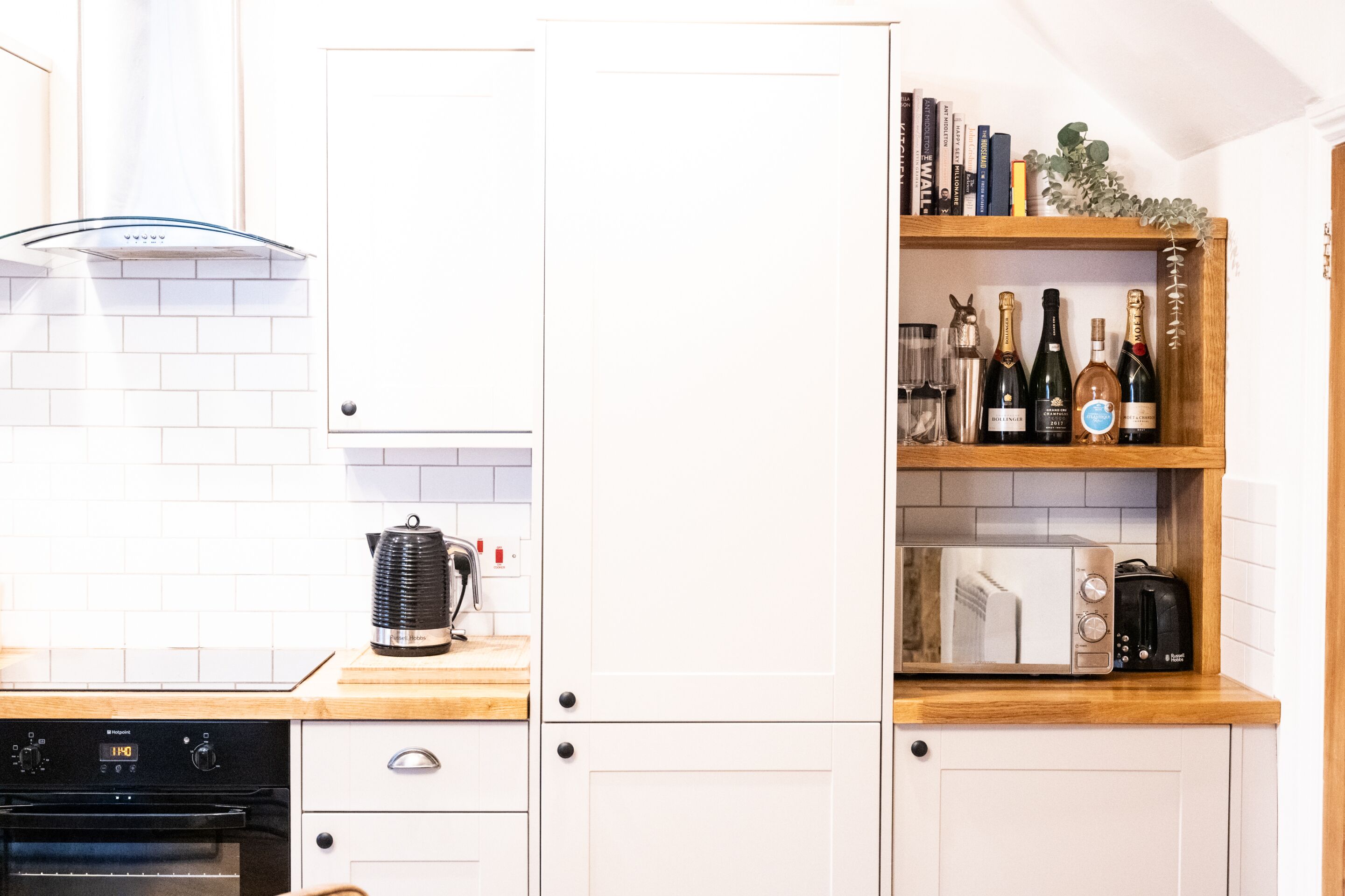 A kitchen with white cabinets, a wooden countertop, a built-in microwave, a coffee maker, and a wine rack with bottles.