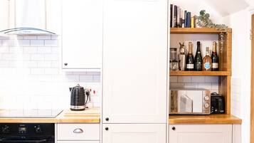 A kitchen with white cabinets, a wooden countertop, a built-in microwave, a coffee maker, and a wine rack with bottles.