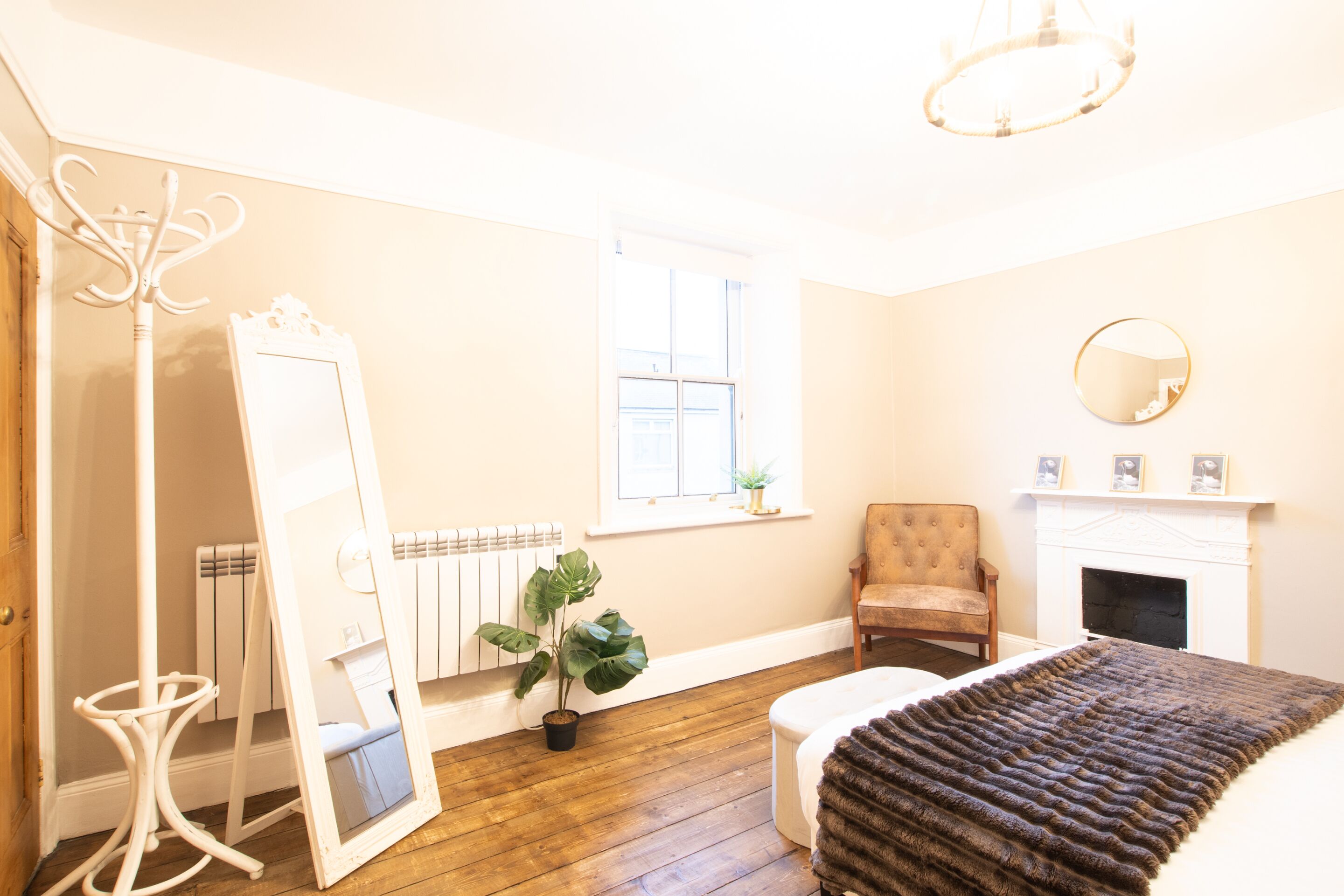 A room with a bed, a chair, a mirror, a radiator, a window, and a fireplace.