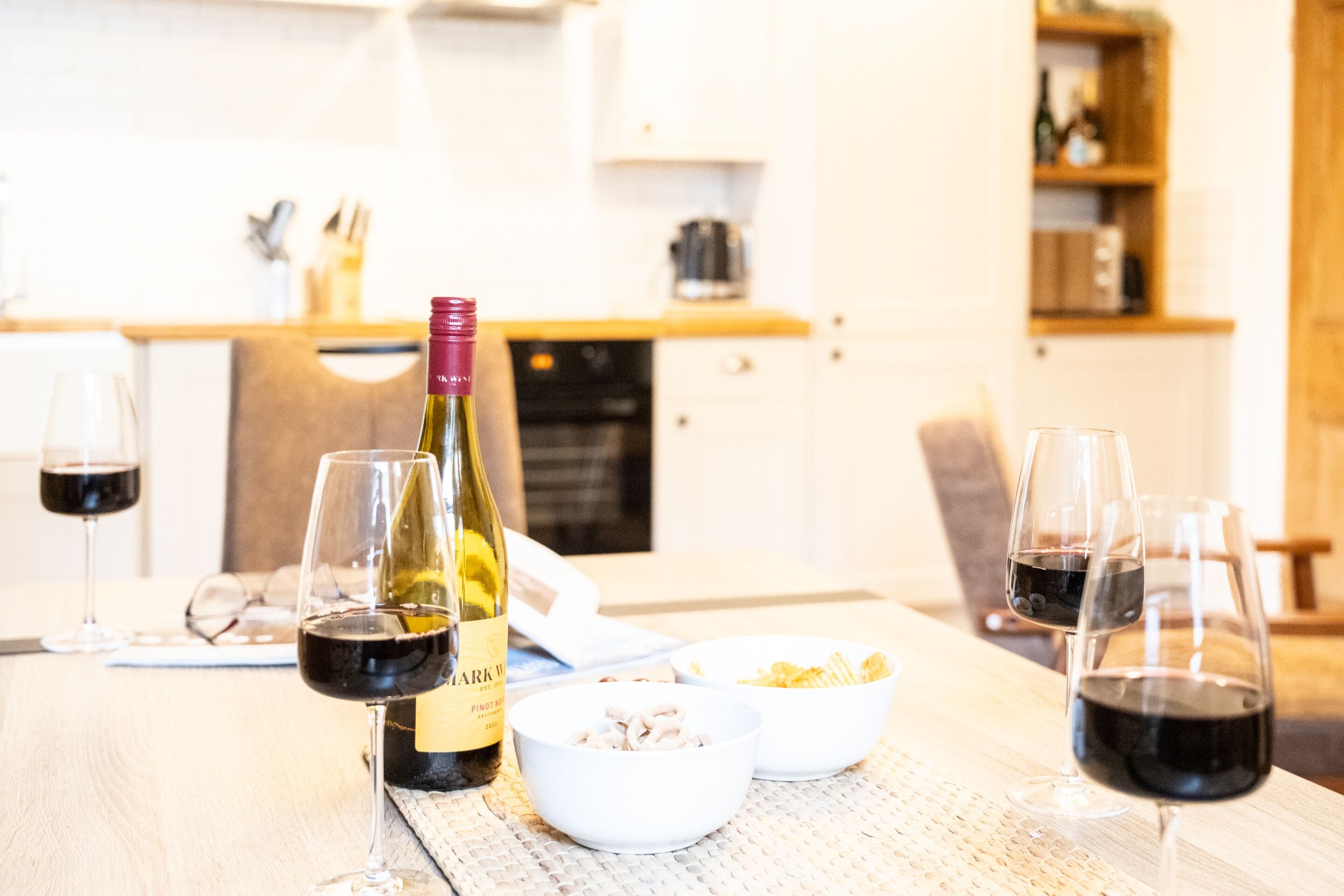 A dining table with wine glasses, a bottle of wine, and bowls of food.