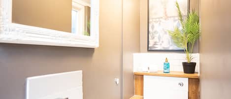 A bathroom with a white sink, a mirror, a framed picture on the wall, and a potted plant.