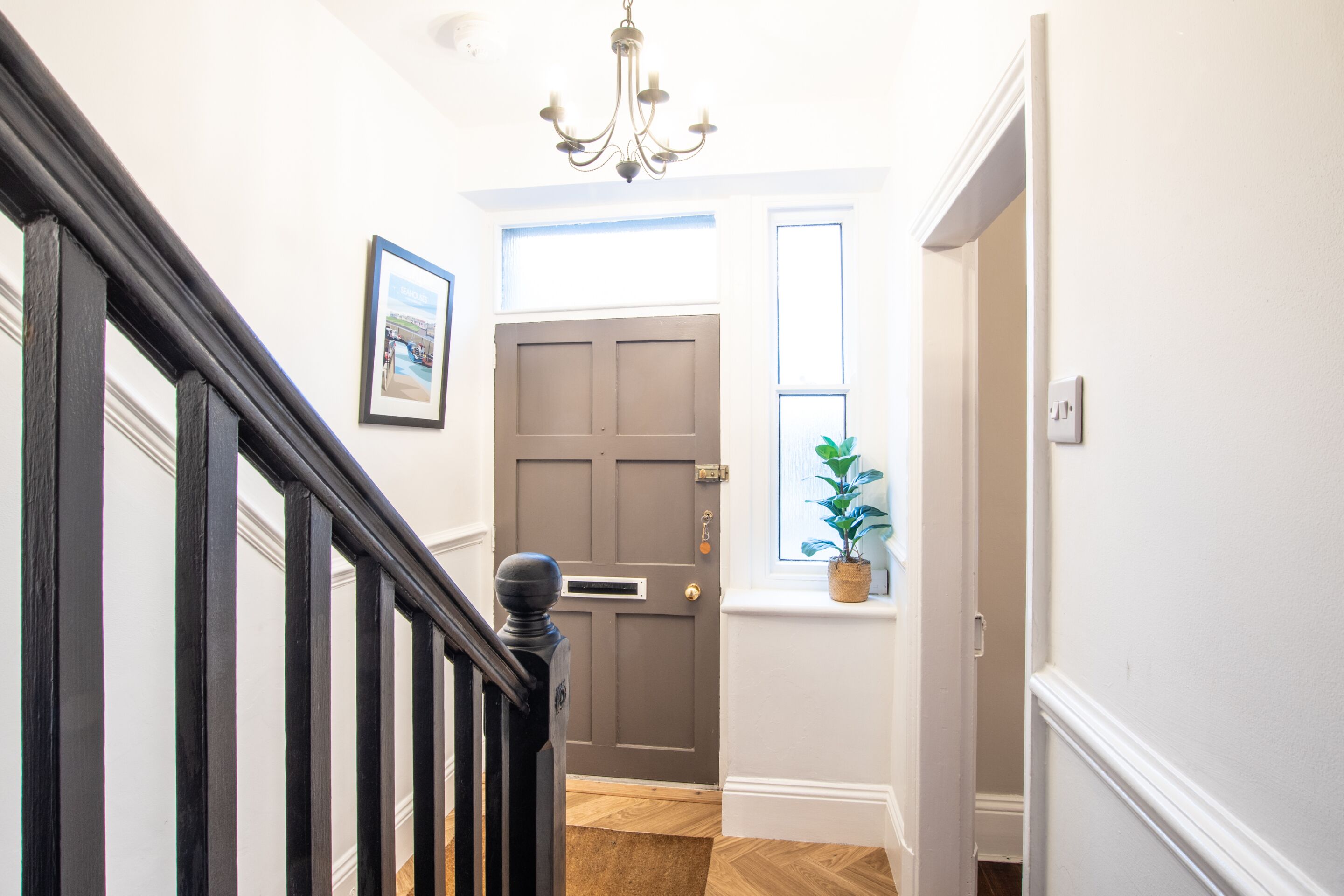 A hallway with a dark wooden staircase, a door with a window, and a plant on the windowsill.
